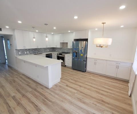 Modern open-concept kitchen with white cabinets, island, and stainless steel appliances in Palm Beach home renovation.