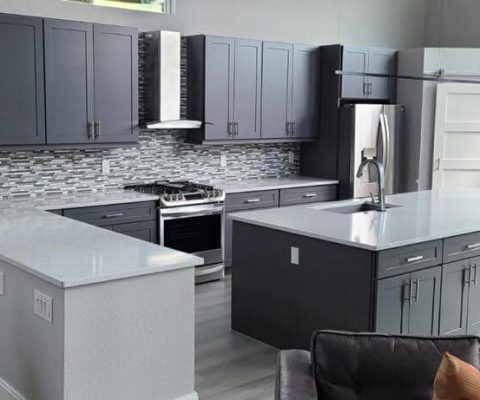 Modern kitchen remodel with sleek gray cabinetry, white countertops, and stainless steel appliances in Palm Beach home renovation.