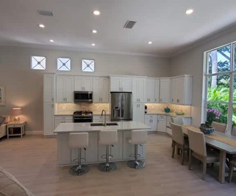 Modern open-concept kitchen with white cabinetry and island seating, featuring stainless steel appliances and large windows, perfect for Palm Beach custom kitchen remodeling and renovation projects.