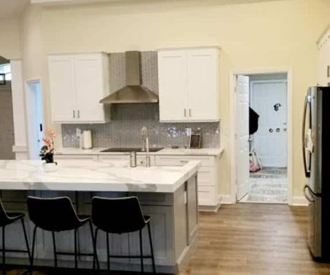 Modern kitchen remodel in Palm Beach showcasing a spacious island with seating, sleek white cabinetry, stainless steel appliances, and elegant wood flooring. Ideal for custom renovation inspiration.